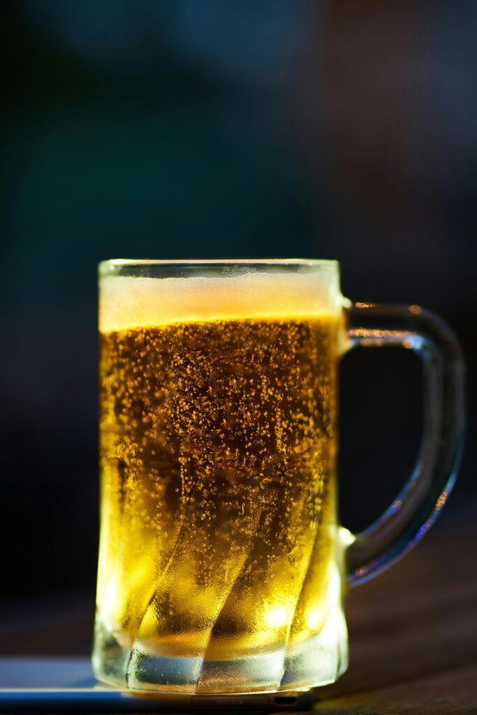 A glass mug of cold beer with frothy head and bokeh lighting effect in a dim setting.